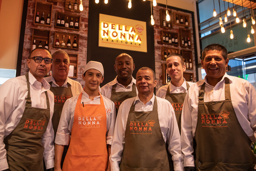 A group of workers smile and pose in front of a restaurant sign that reads 'Della Nonna'