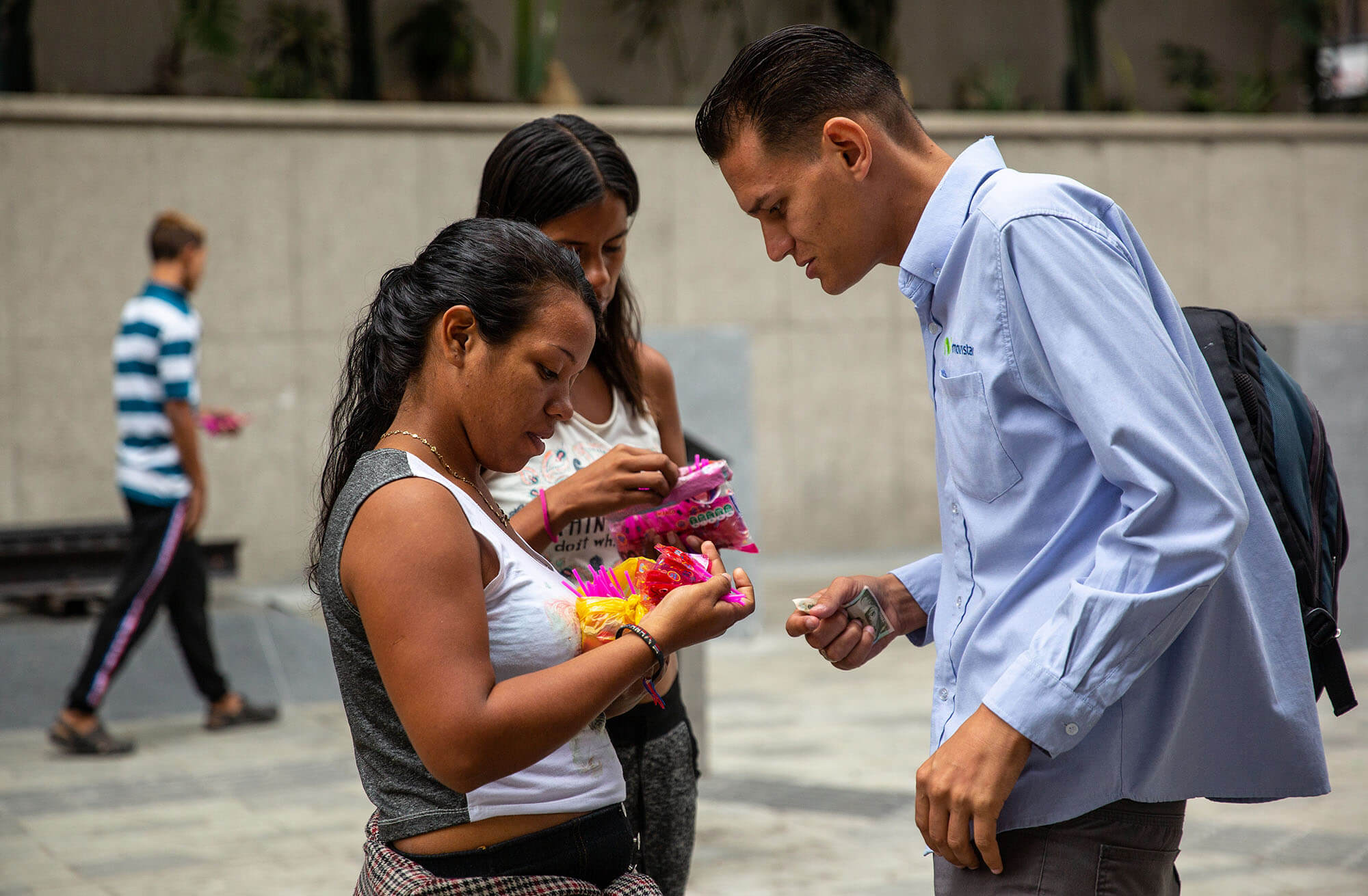 Two women show a man small candy they are giving out while he grips money