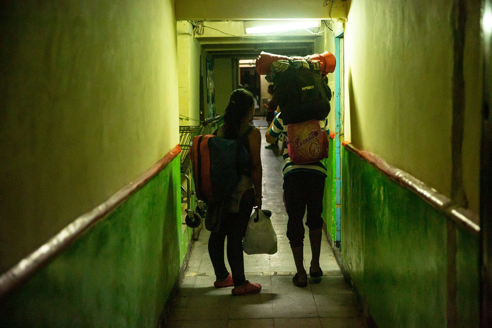 A man and a woman stand in a dimly lit green hallway