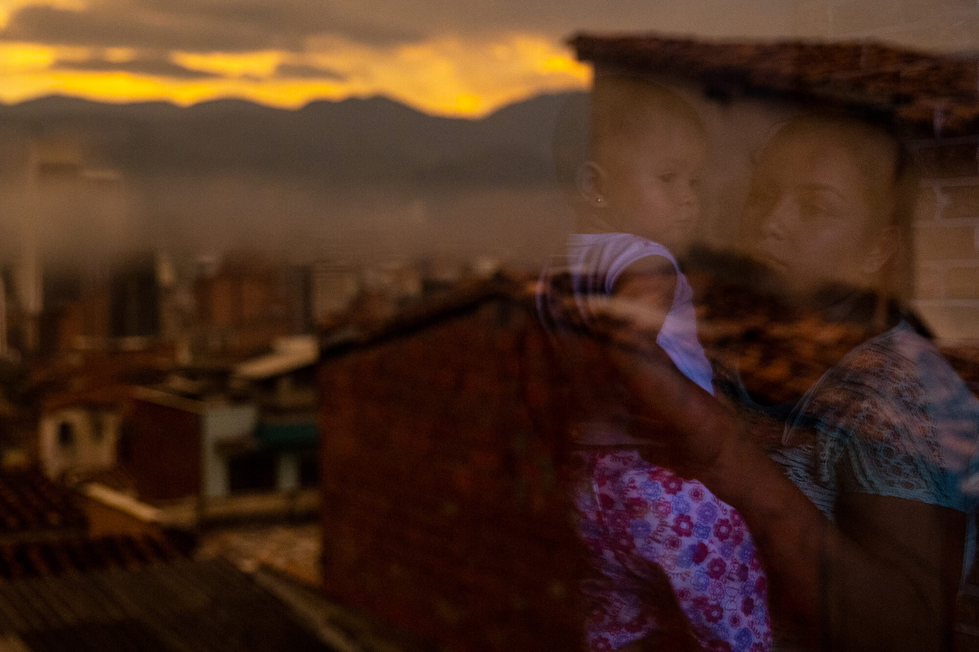 A mother holding her baby is reflected in a window overlooking a city skyline