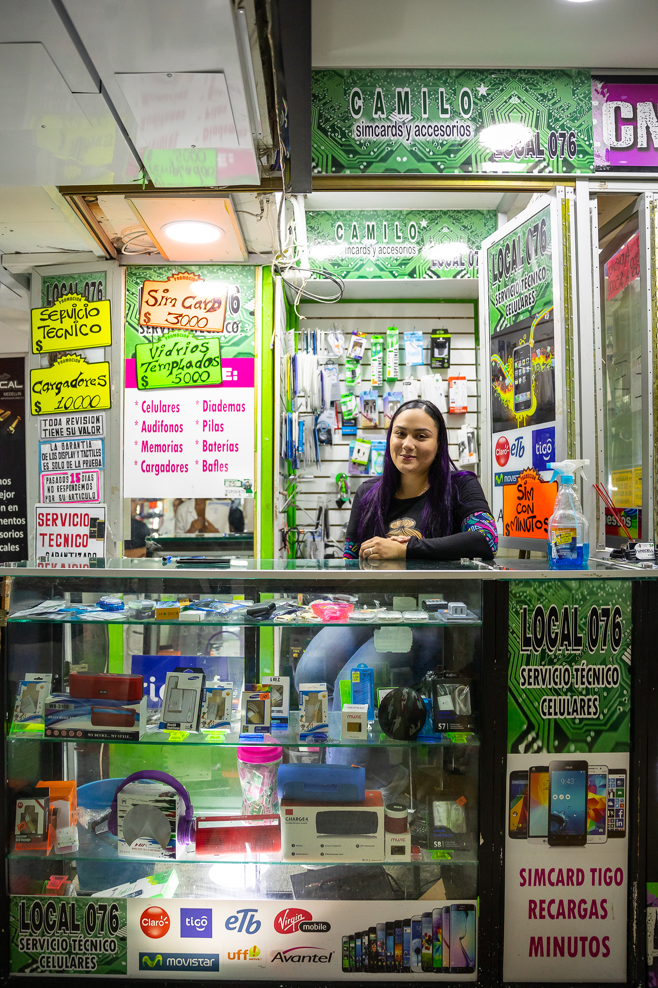 A woman sits in her cell phone shop in a mall, framed by all of the products around her