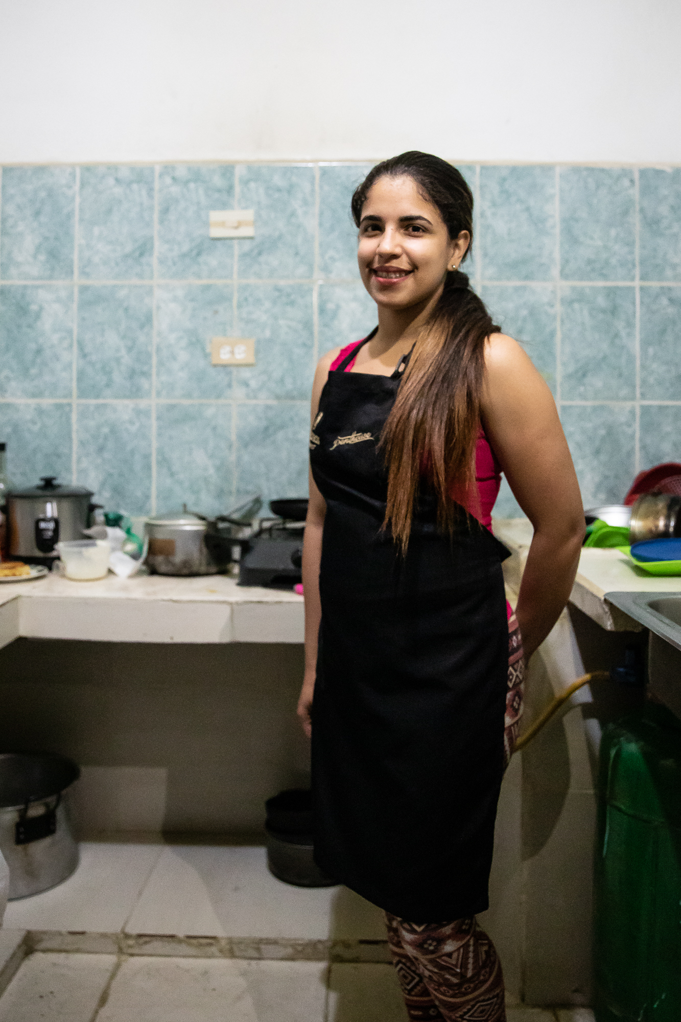 A woman wearing an apron poses for a portrait in her kitchen