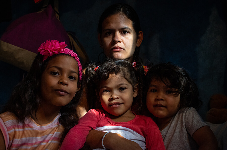 A woman sits on her bed holding her three children