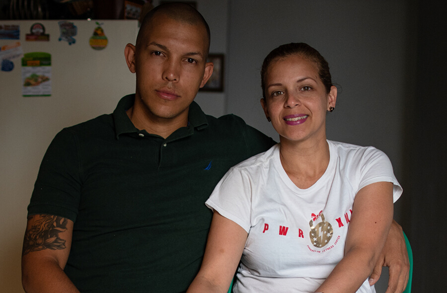 A husband and wife sit together in their home smiling