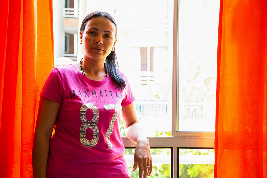 A woman stands in front of a bright window and orange curtains