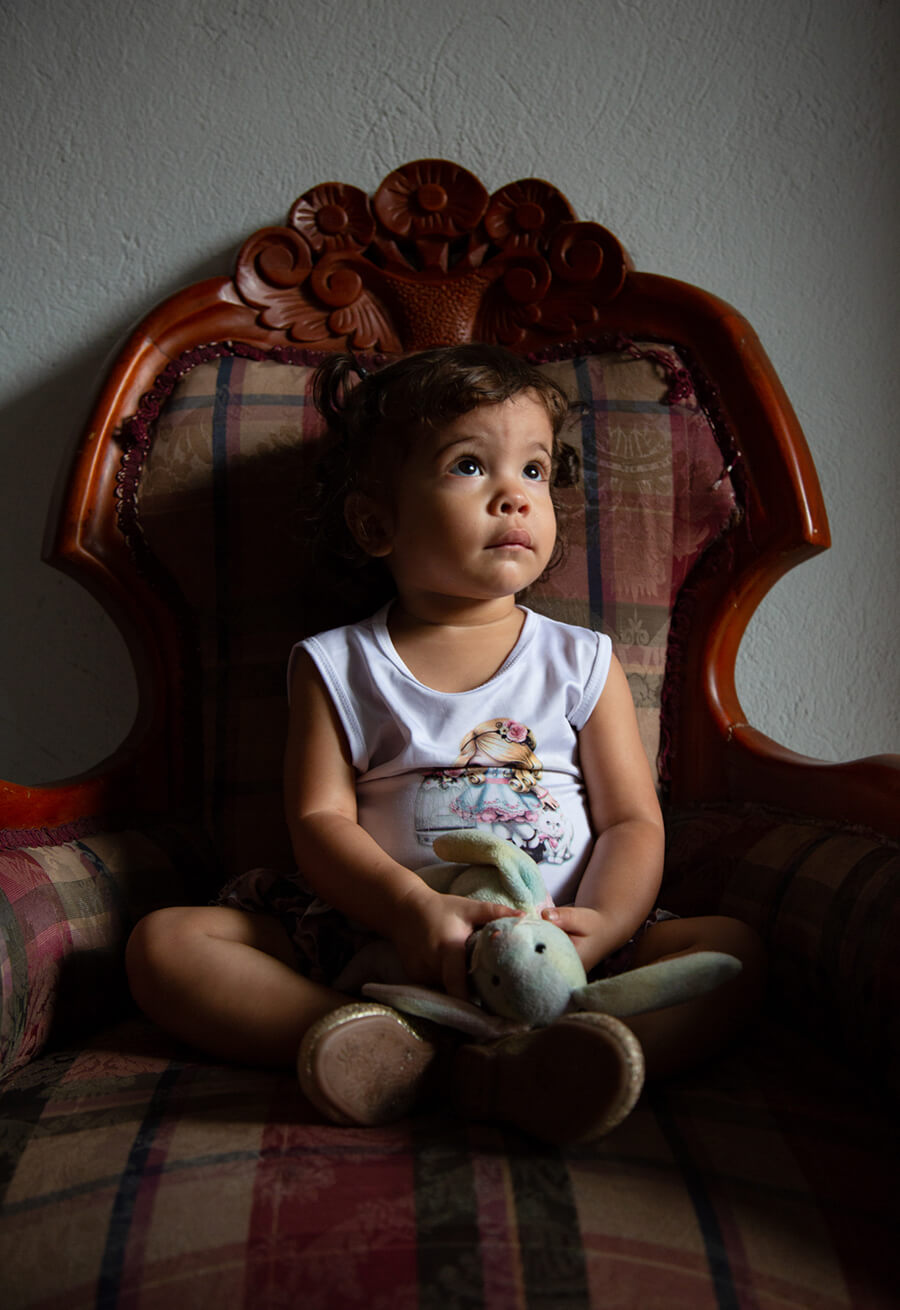 A young girl sits in a large chair holding her favorite stuffed animal, a bunny